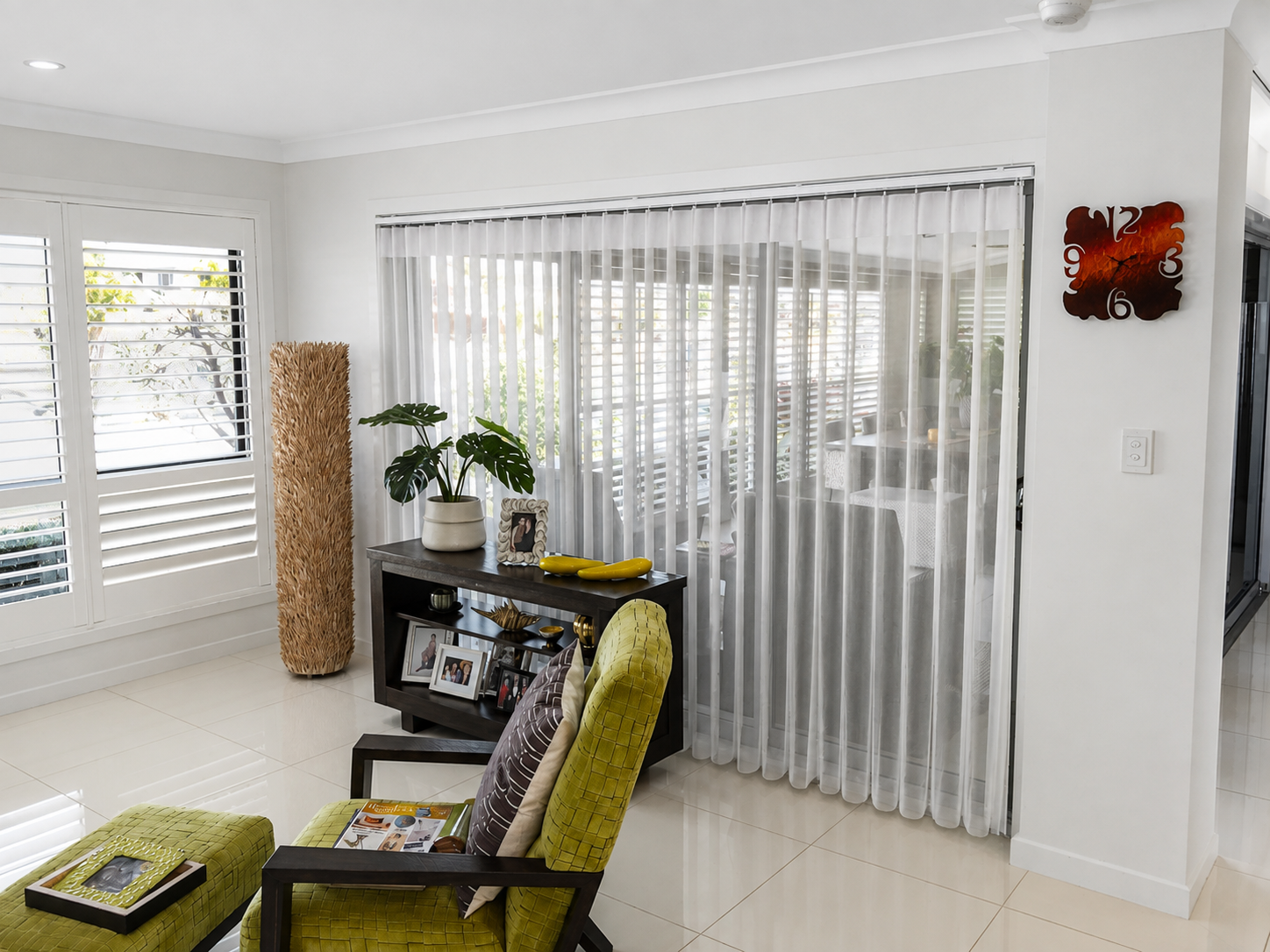 White Veri-shade blind in lounge with cream tiled floor and white plantation shutters in window 
